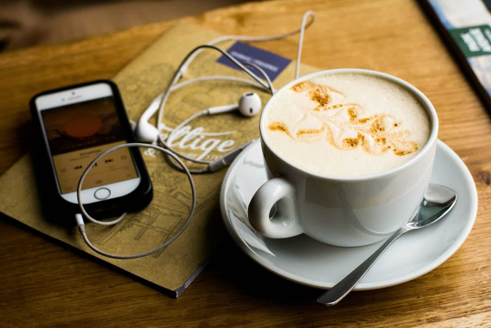 coffee with podcast playing next to it on wooden table
