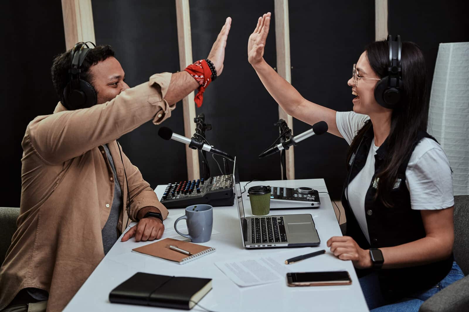 Portait of two cheerful radio hosts, young man and woman giving high five while talking, moderating a live show in studio. Side view. Selective focus. Horizontal shot